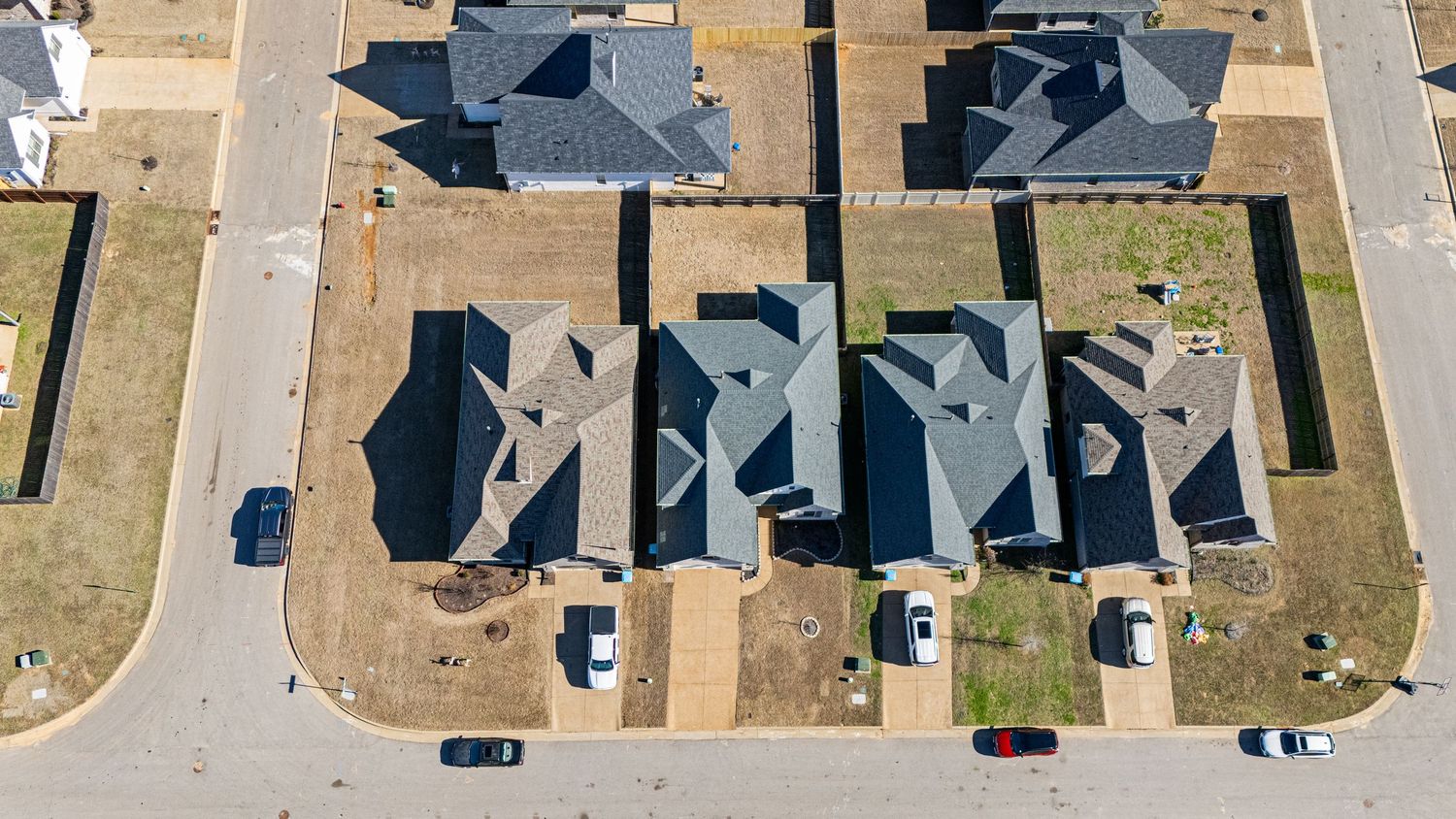 Aerial view of suburban neighborhood with beige houses and driveways arranged in rows along residential streets.