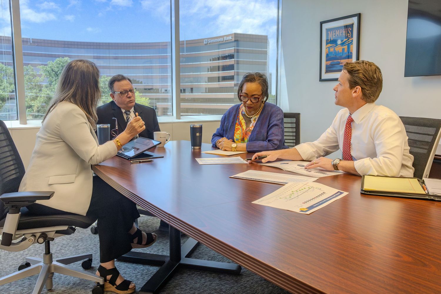 Meeting participants seated around a wooden conference table near large windows.