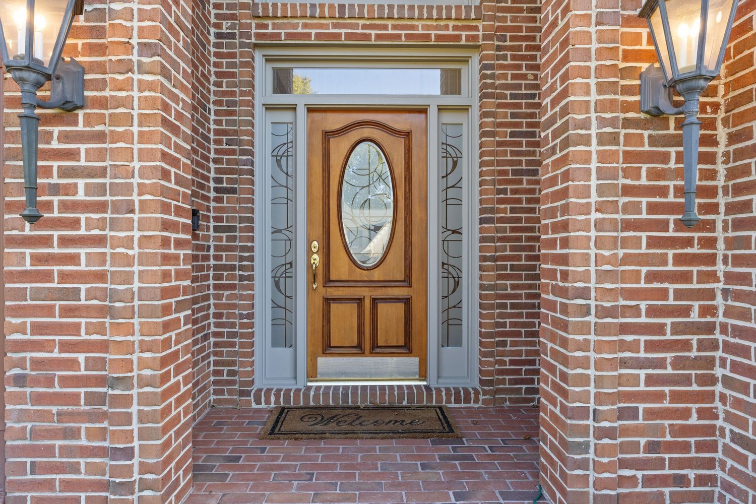 Decorative wall sconces illuminate a brick wall hallway with wooden doors and oval windows.