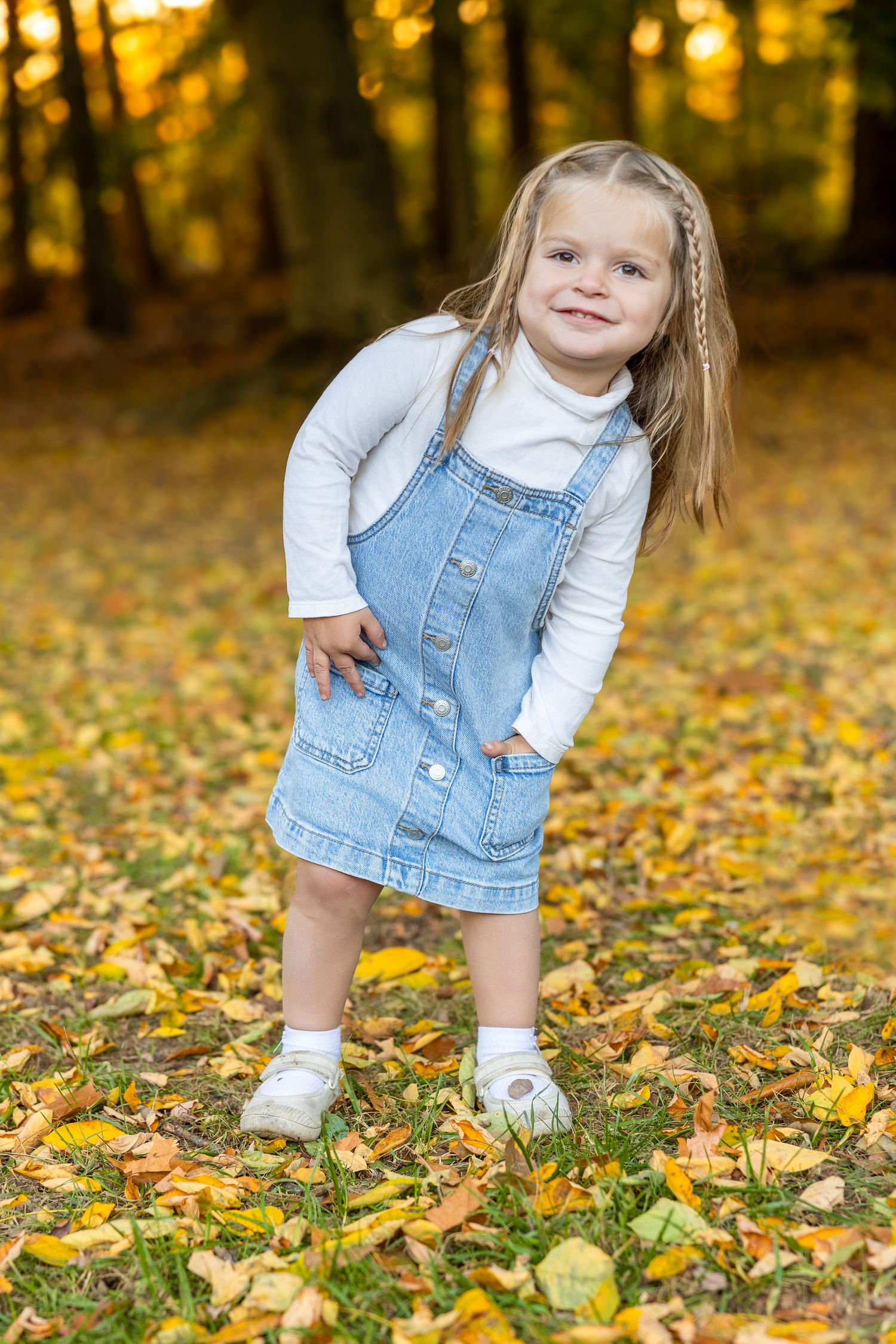 Child in denim overalls playing among fallen autumn leaves.