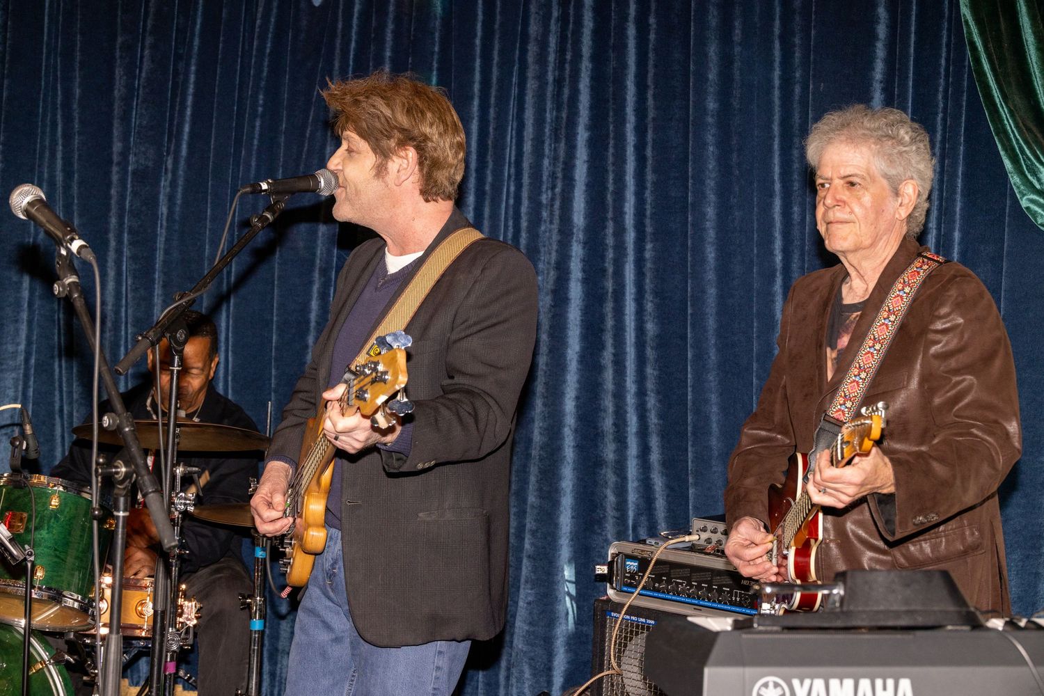 Band members performing with guitars and other instruments on a stage.