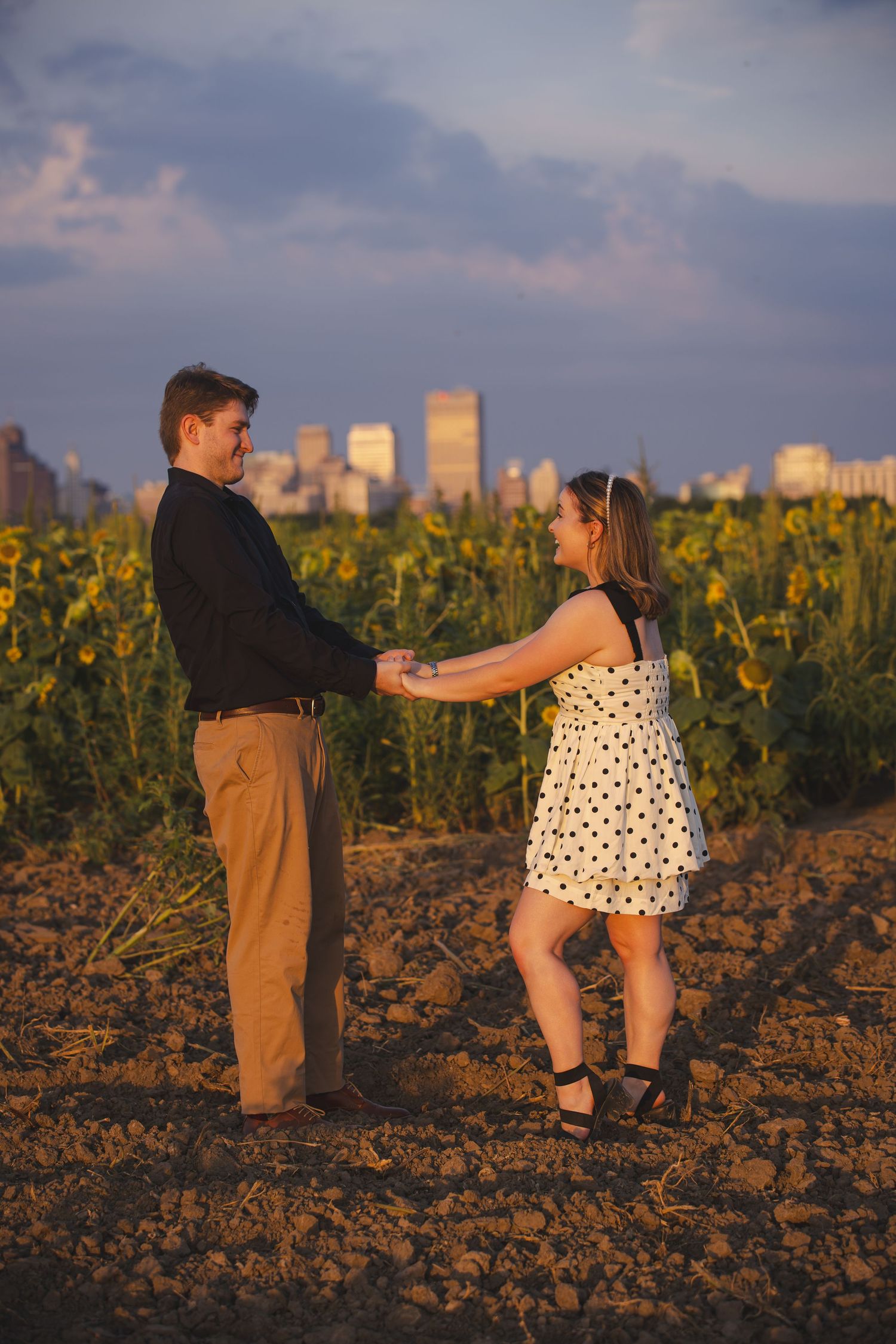 Playful dance sequence in sunflower field with city skyline visible.