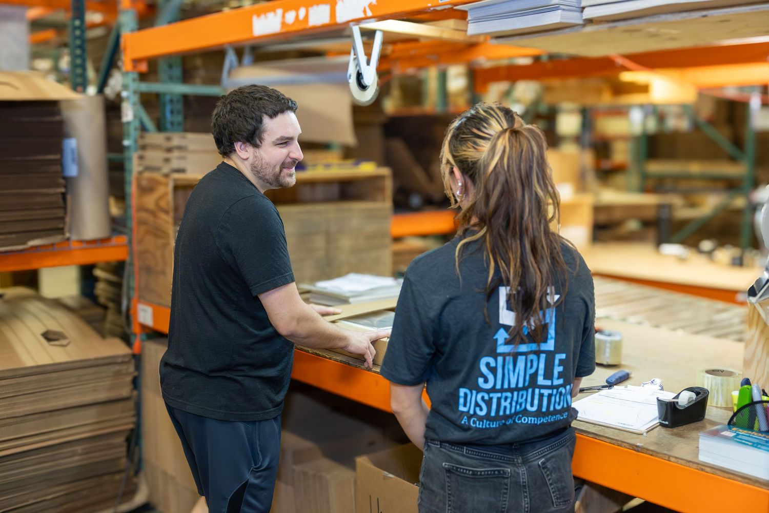 Workers collaborating in a warehouse fulfillment center with orange storage racks.