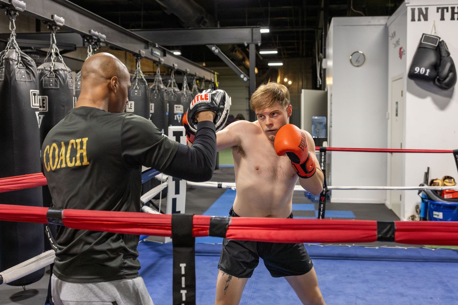 Boxing training session with coach holding pads in professional gym ring.
