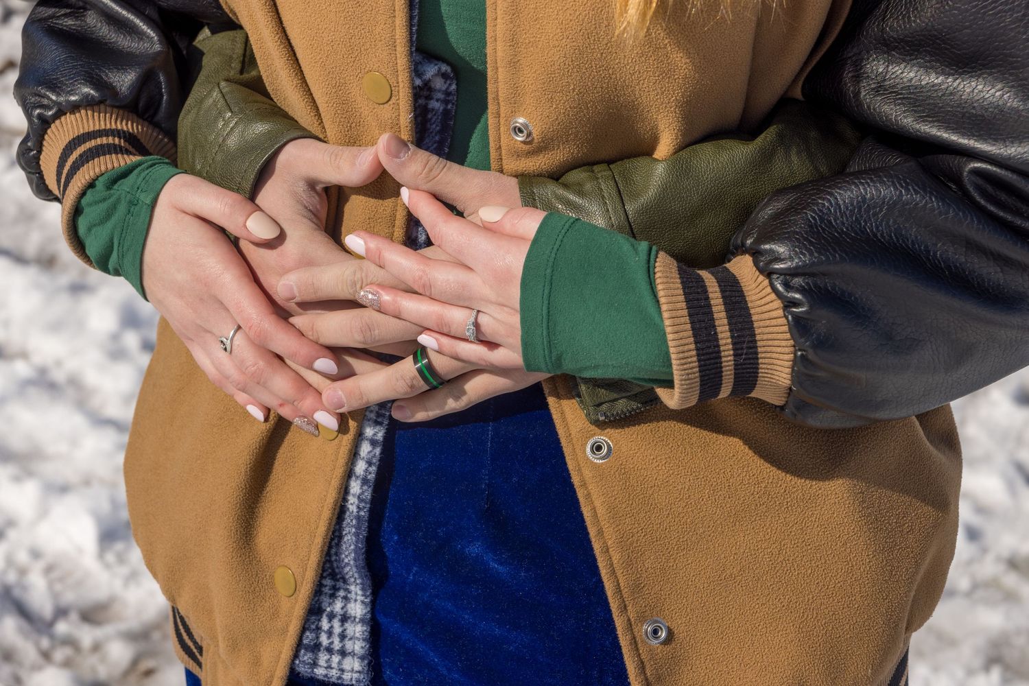 Detail shot of hands displaying engagement rings against winter clothing.