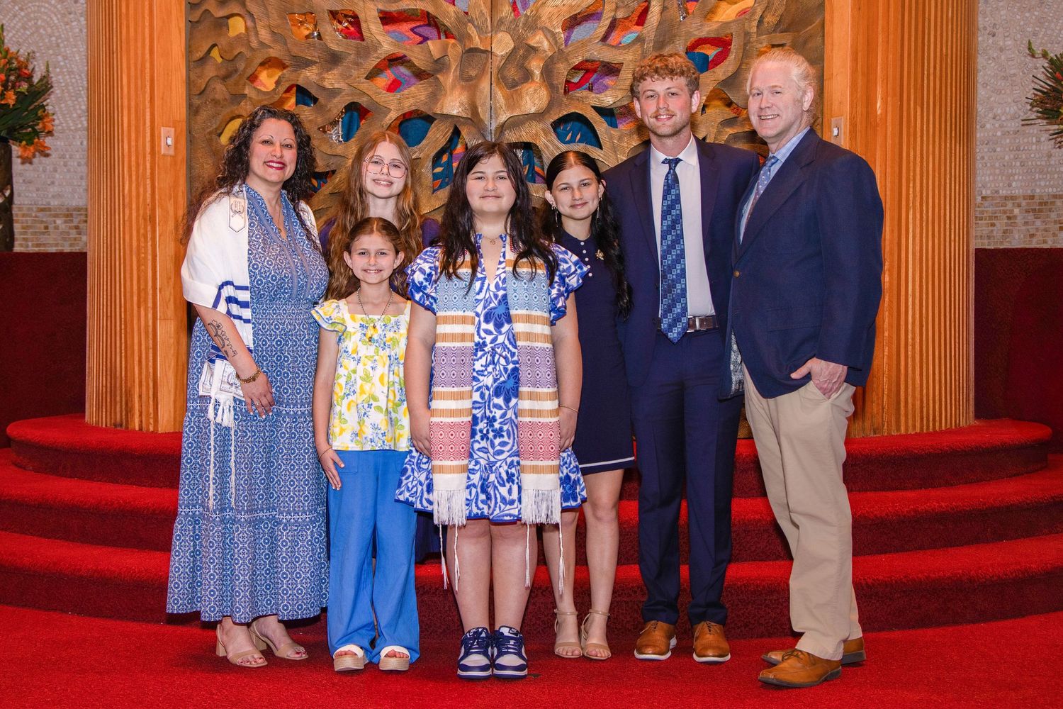 A group of people standing together on red carpeted church steps in formal attire.