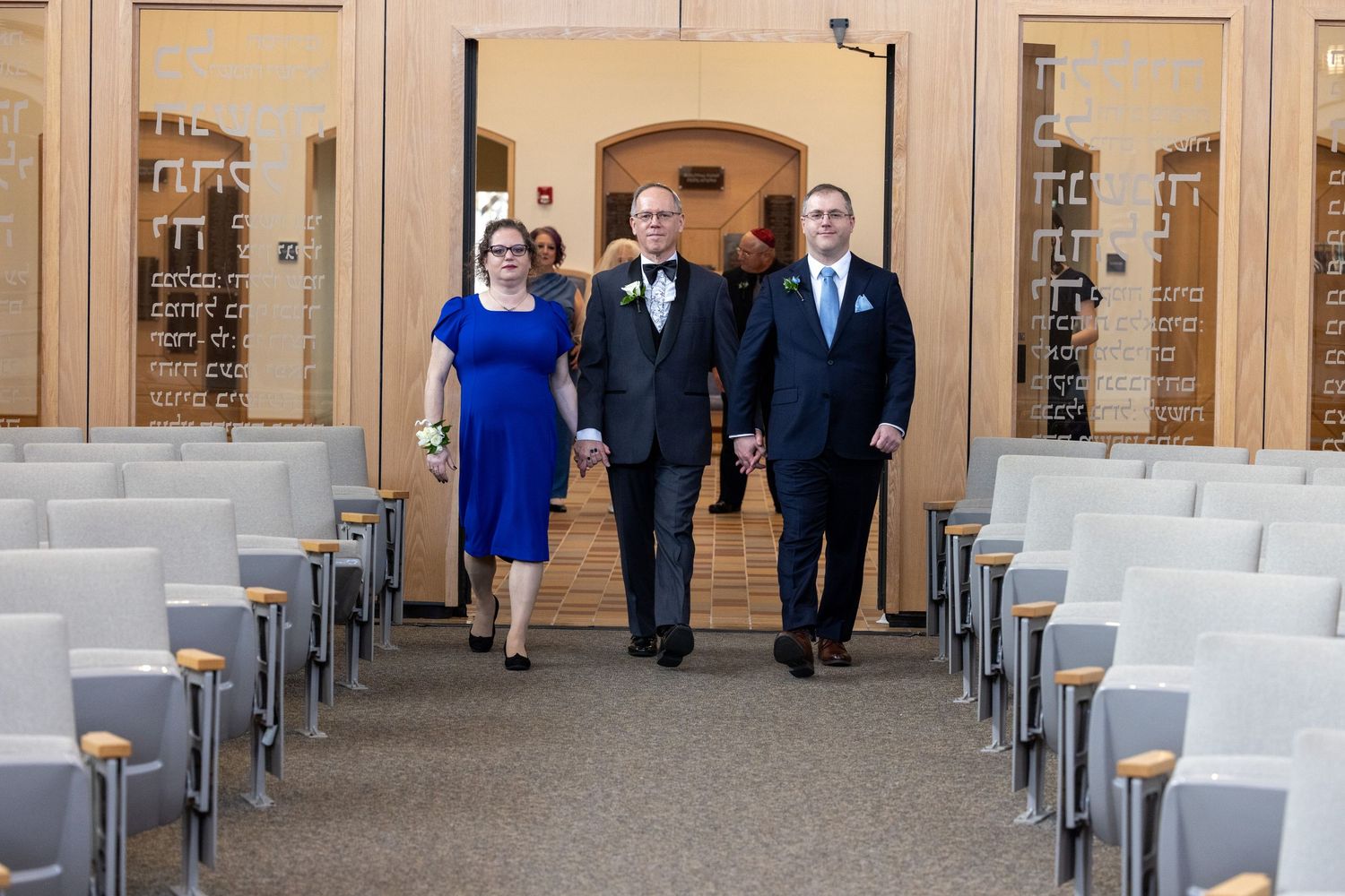 Wedding guests walk down an elegant colonnade hallway lined with white chairs for an outdoor ceremony.