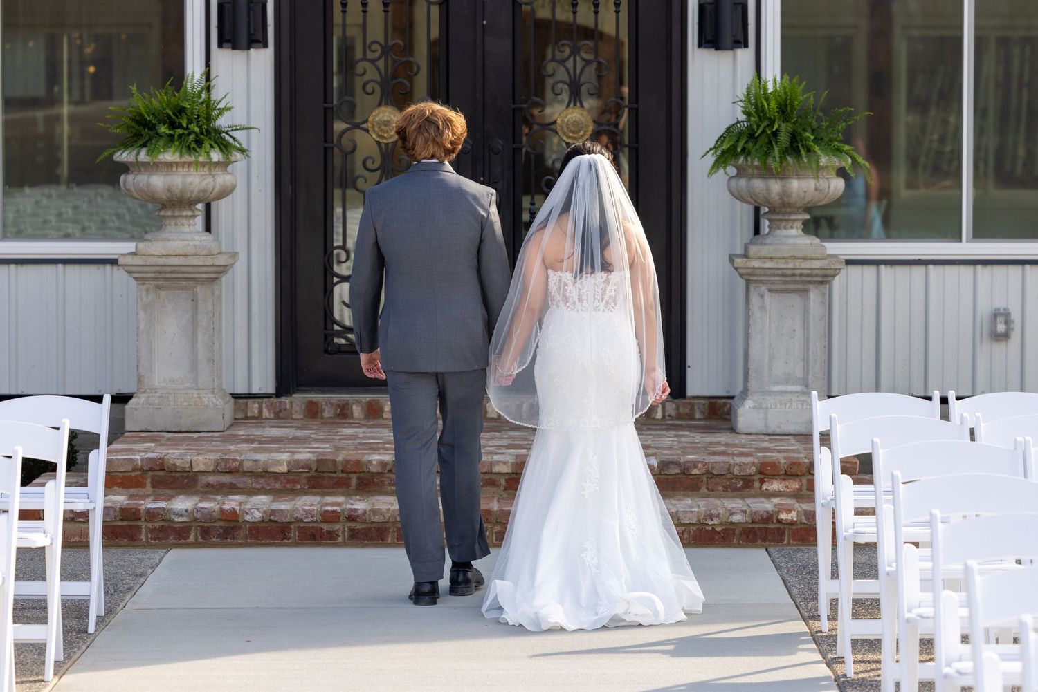 A panoramic view of an elegant outdoor wedding ceremony setup with white chairs and decorative greenery.