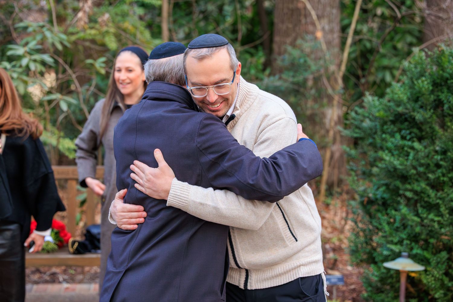 People embracing and hugging each other outdoors in a garden or park setting.