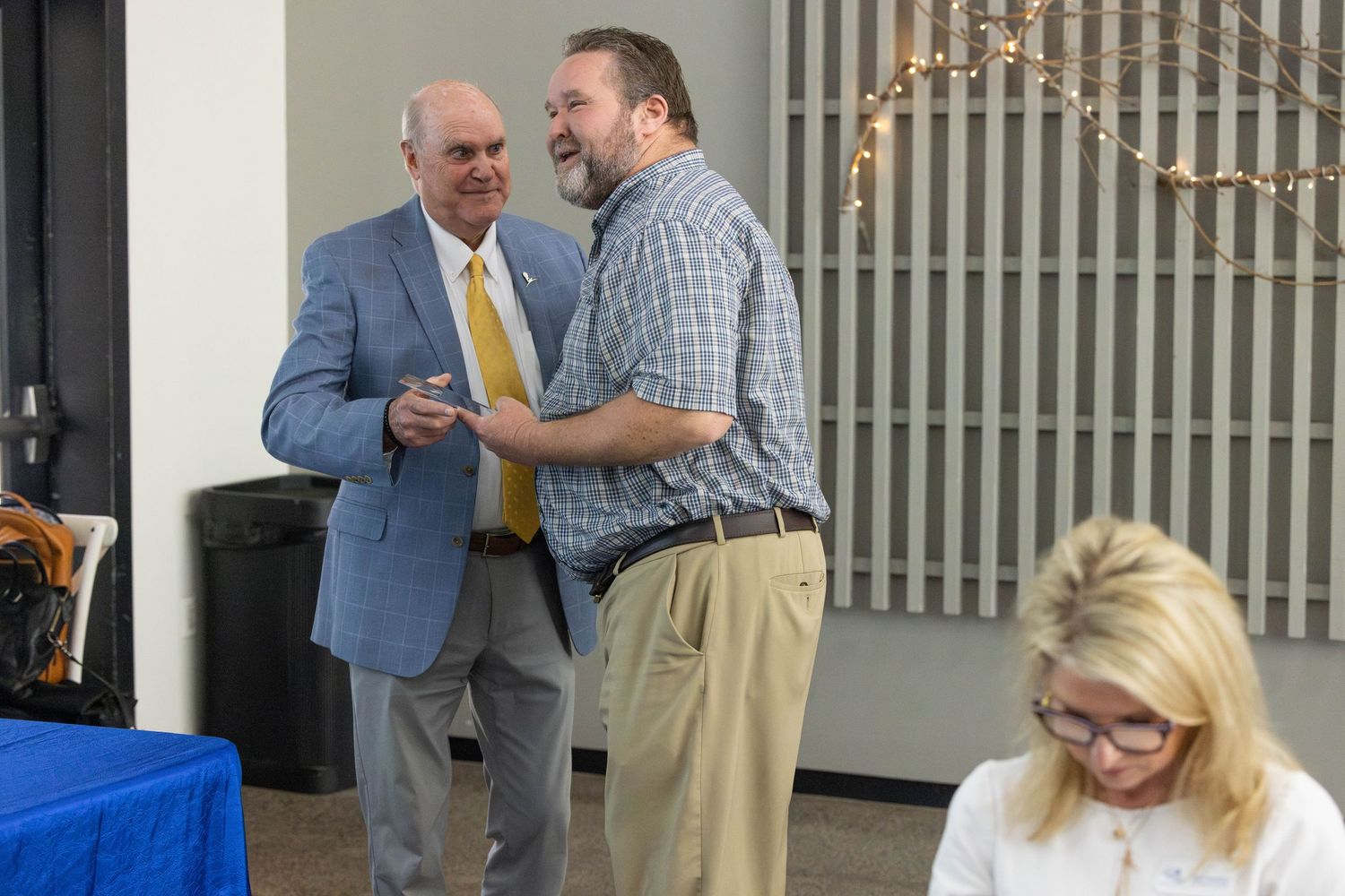 Business professionals engage in conversation while standing in a modern office hallway.