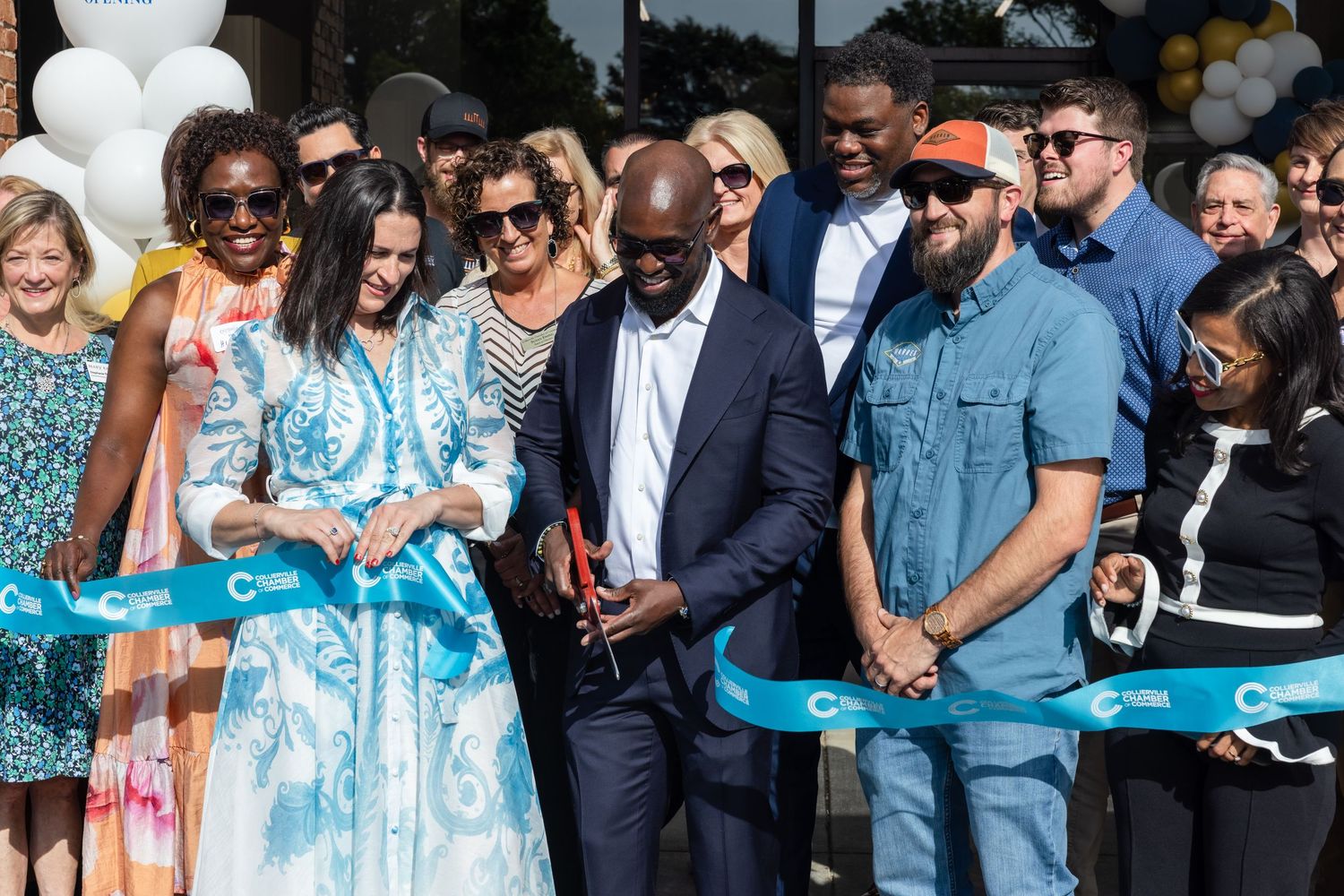 Group of people at a ribbon cutting ceremony outdoors, celebrating a grand opening on a sunny day.