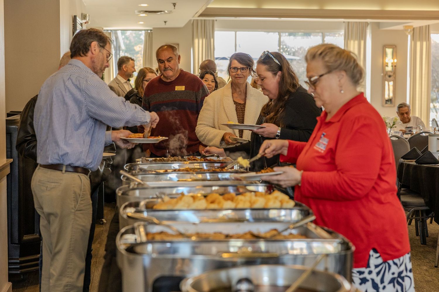 People serving themselves from a buffet line with multiple chafing dishes.