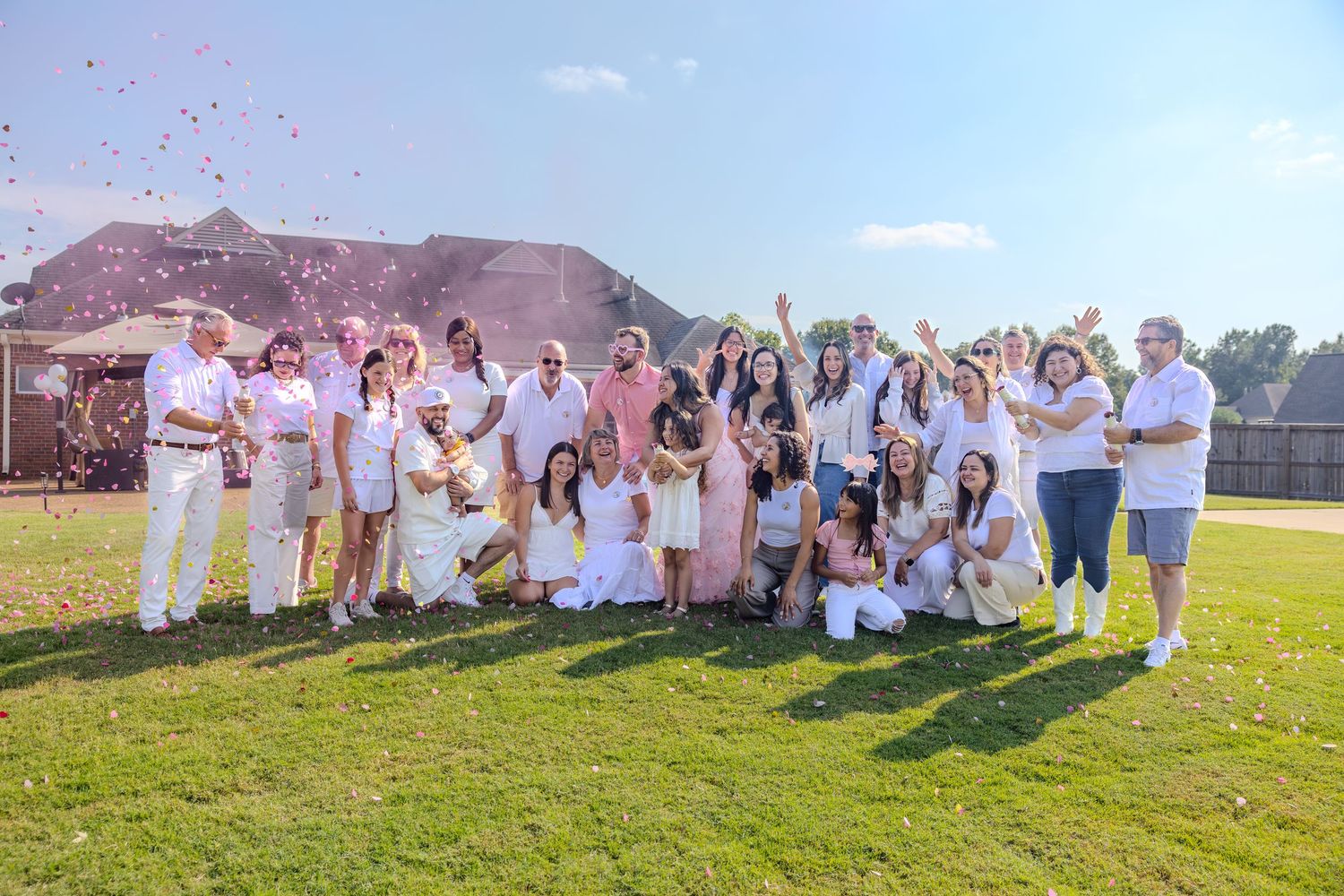 People in white clothing celebrate outdoors with pink powder against a mountain backdrop.