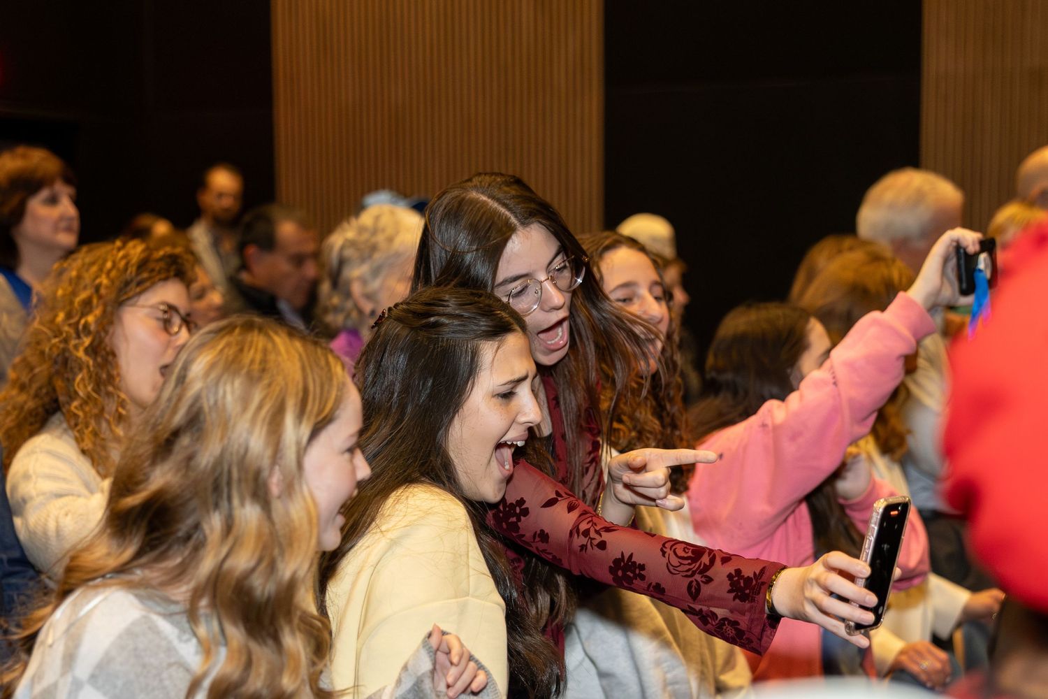 Audience members laugh and react enthusiastically during an indoor event.