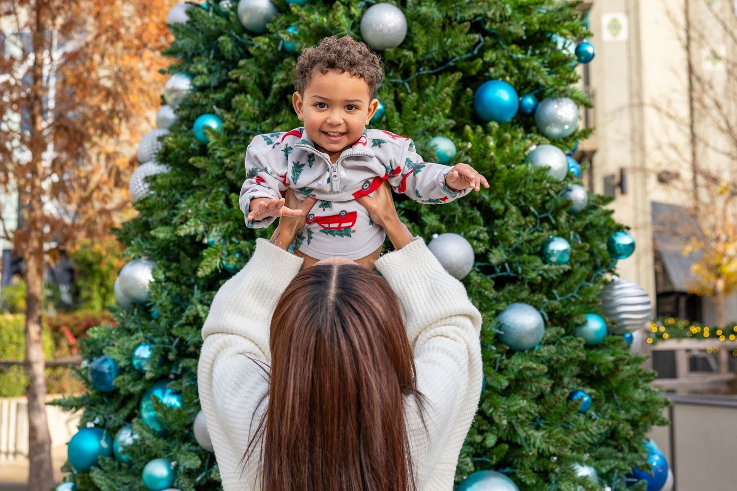 Christmas tree adorned with blue and silver ornaments against autumn foliage.