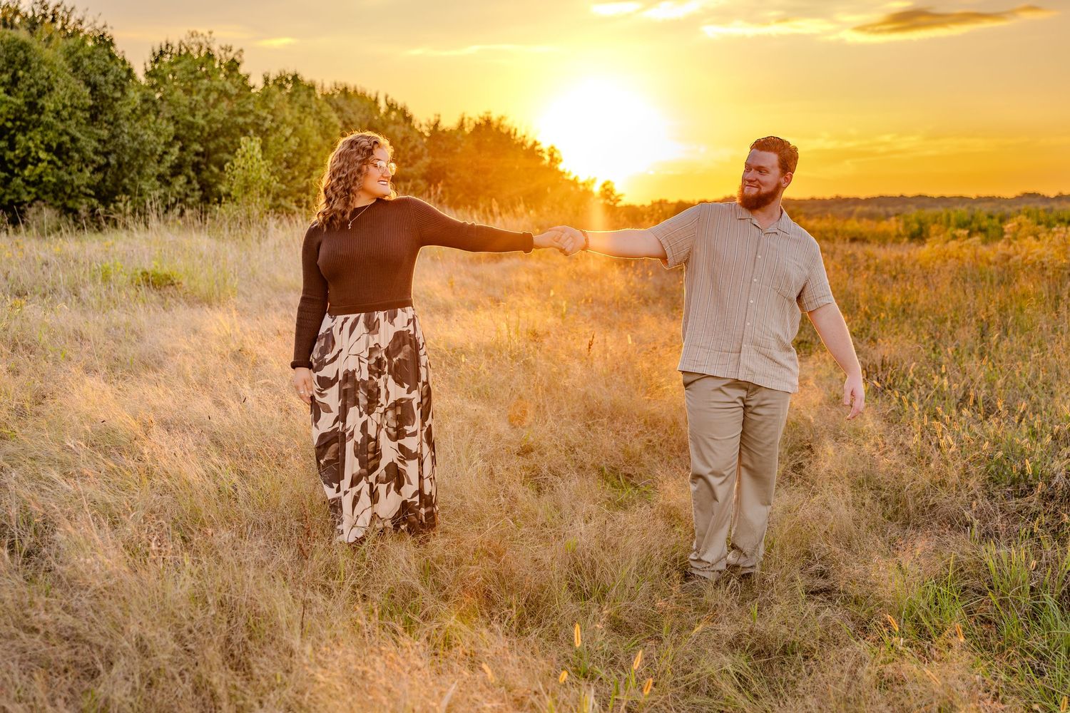 Couple embracing in a golden field at sunset with tall grass and warm lighting.