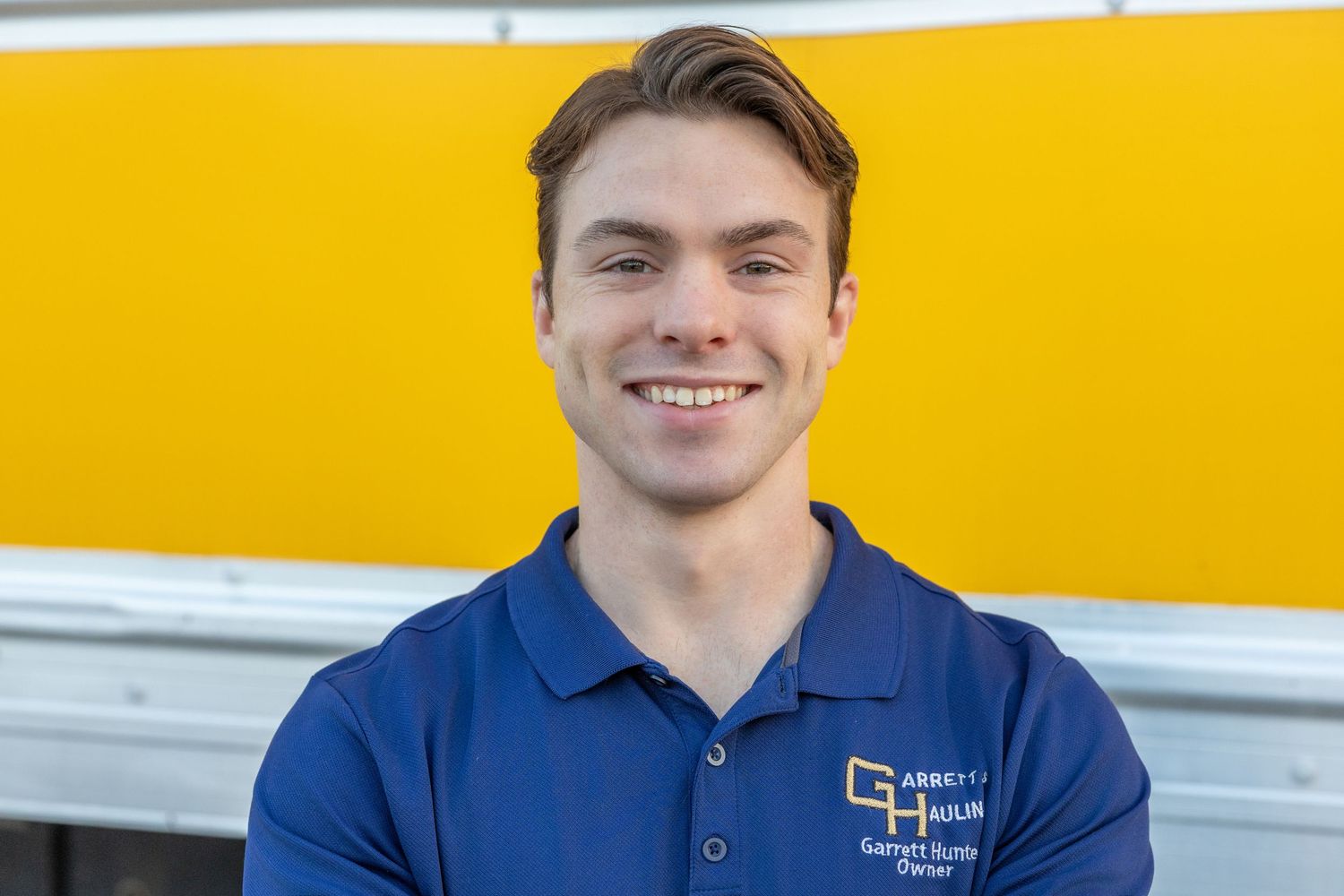 Employee in blue polo shirt with company branding against yellow wall.