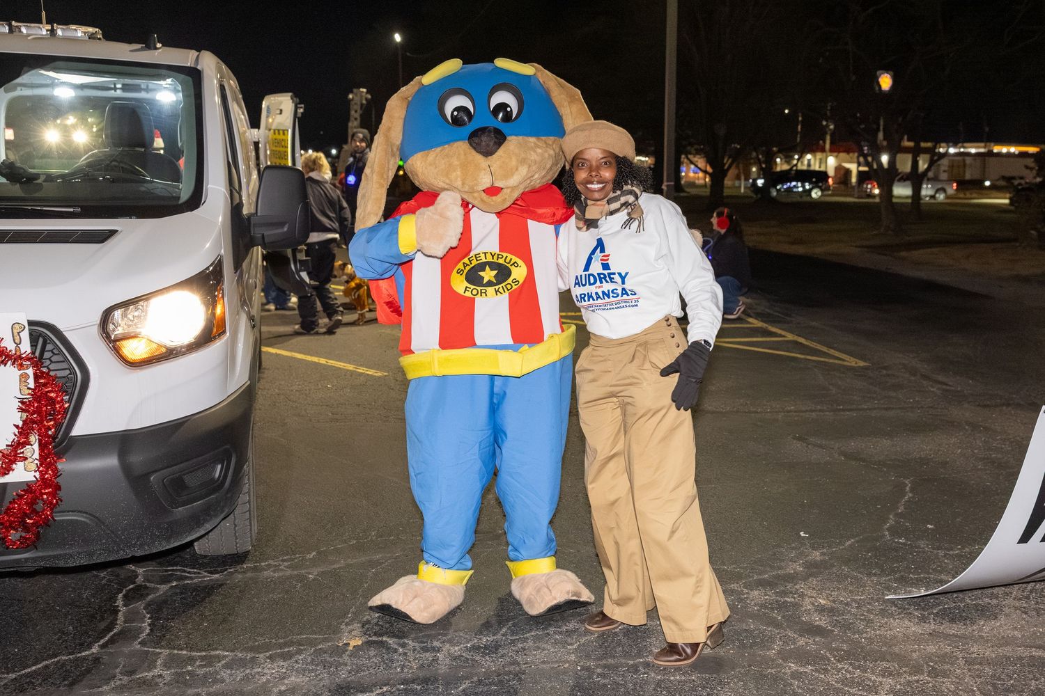 Mascot character in blue overalls poses with attendees at nighttime event.