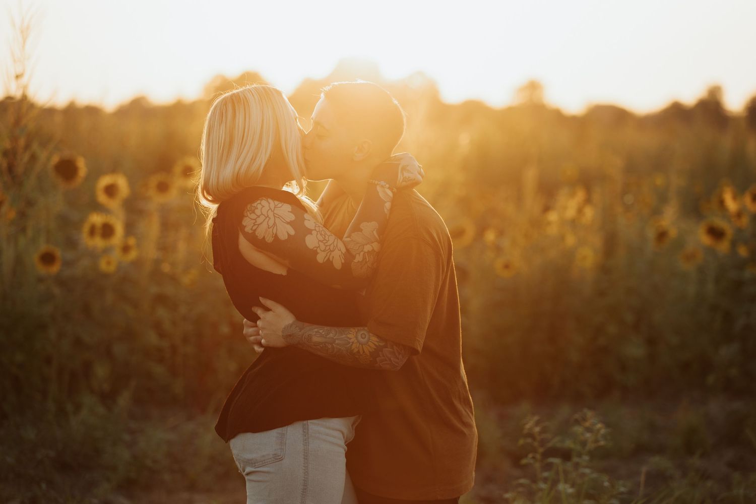 Backlit couple sharing an intimate moment among blooming sunflowers at sunset.