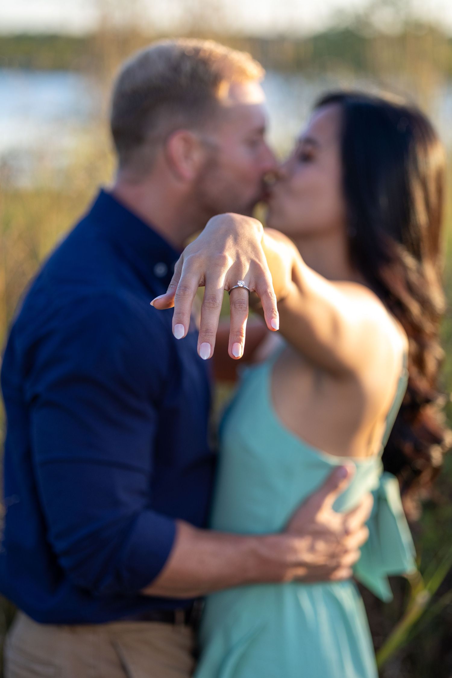 Two people in blue and mint green outfits embrace during a sunset photo session.