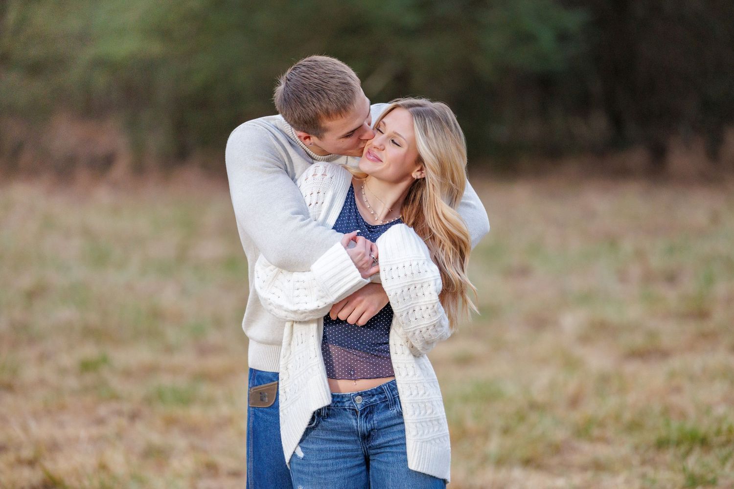Two people embracing in casual wear while standing in a serene outdoor field.