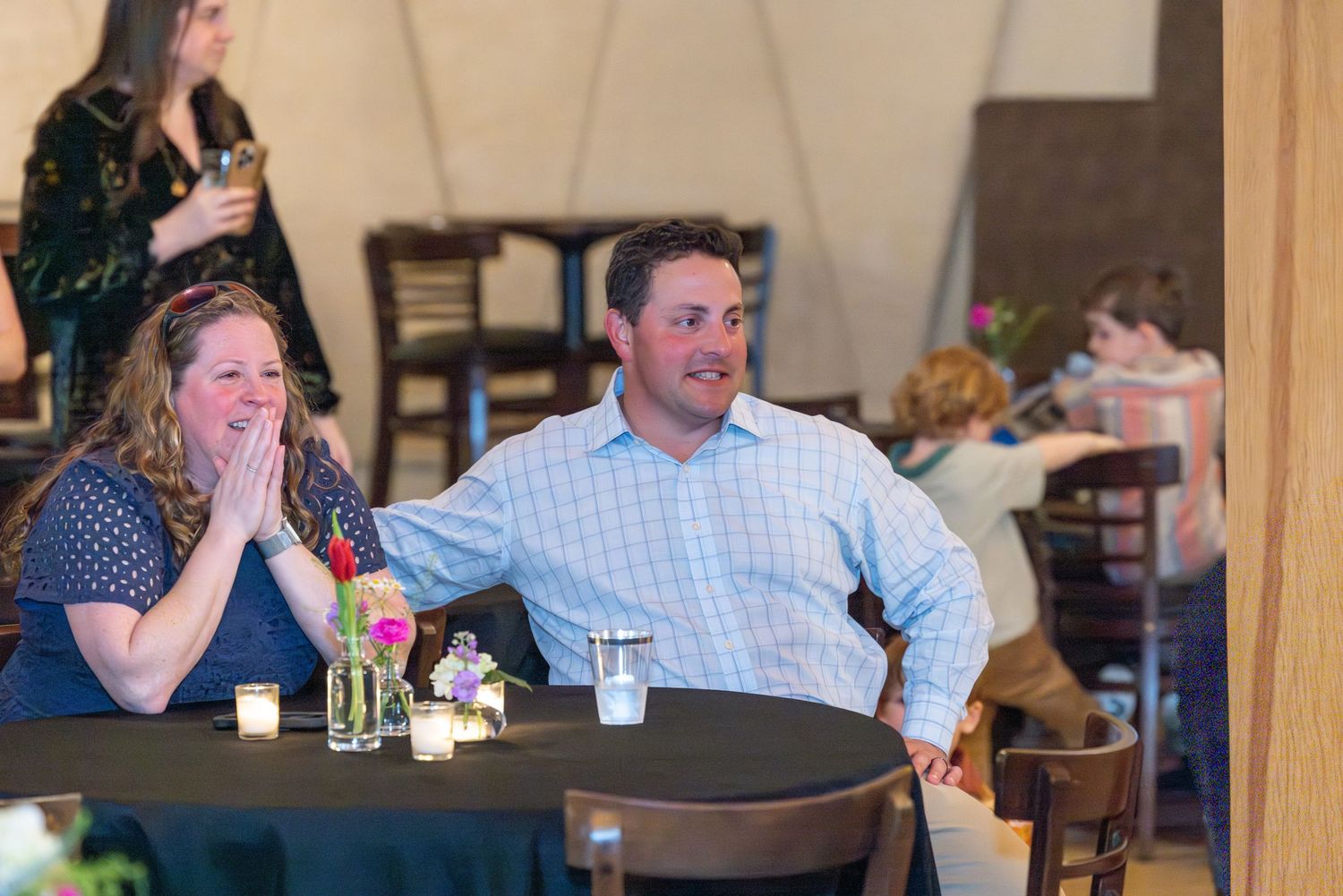 Couple laughing at a table during a surprise party event at a venue.