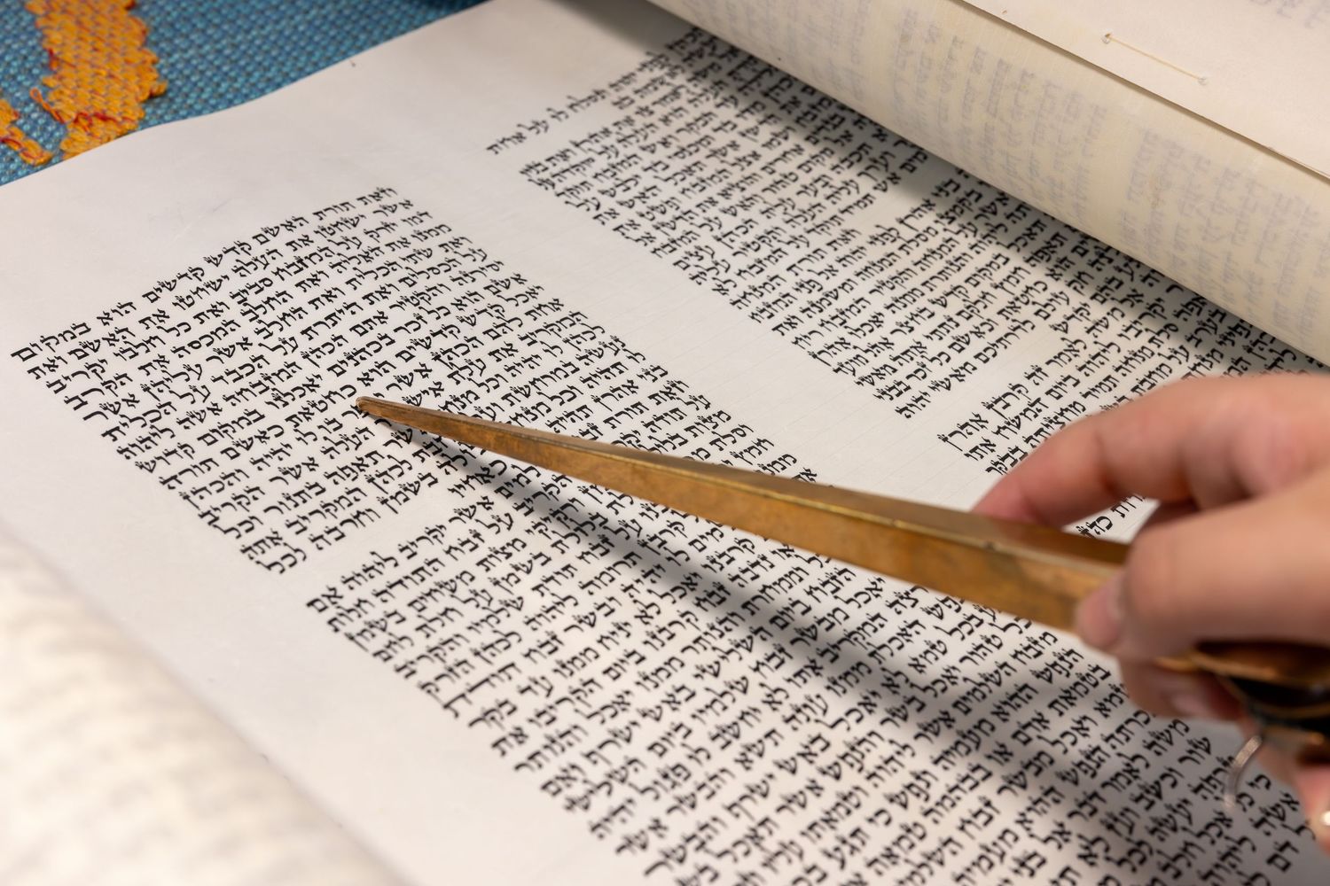 A hand holding a pointer stick moves across lines of Hebrew text in a Torah scroll during a reading.