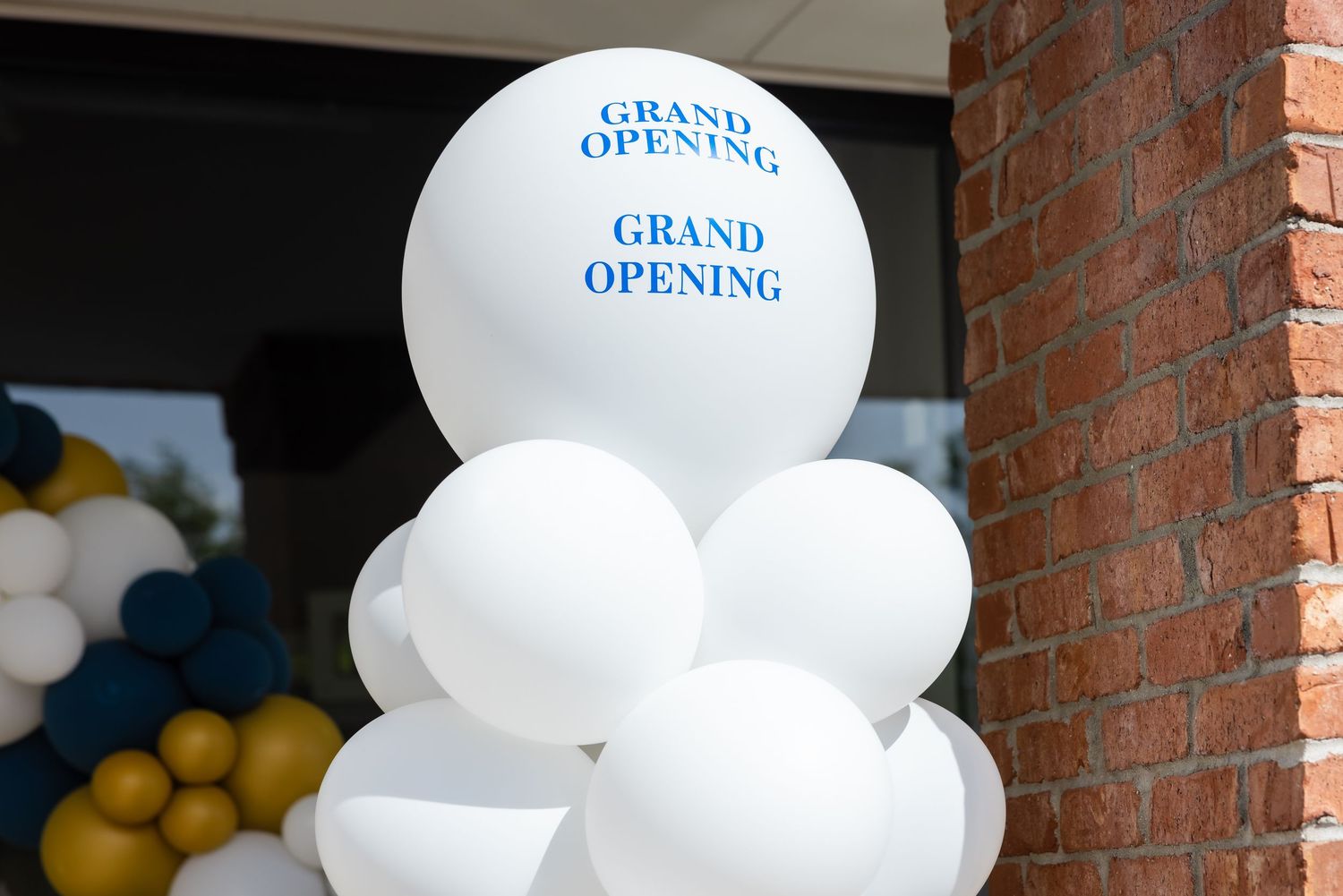 White grand opening balloons arranged in a column display outside a brick building entrance.
