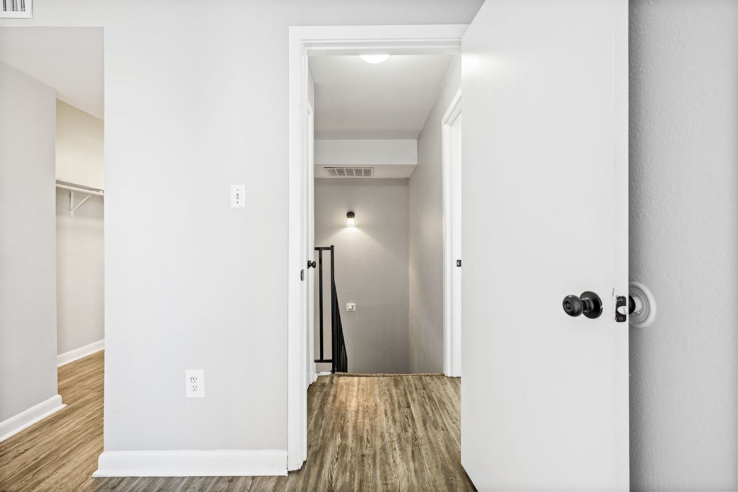 Modern apartment hallway with white walls, hardwood floors, and recessed lighting leading to multiple rooms.