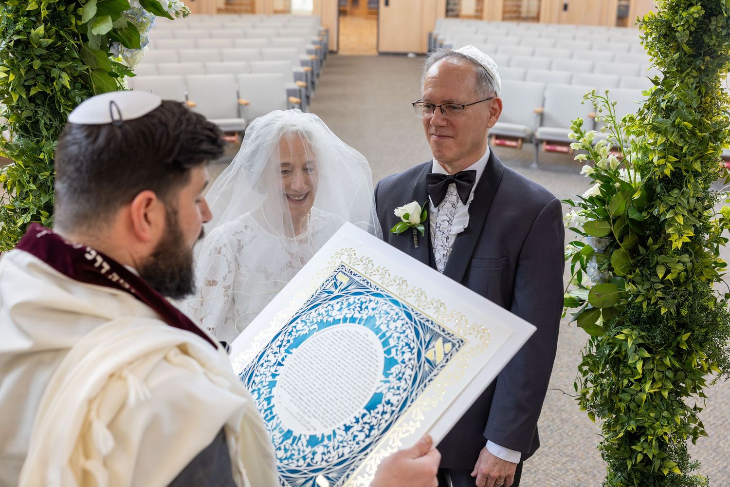 A couple signs a marriage certificate during an outdoor wedding ceremony surrounded by greenery.
