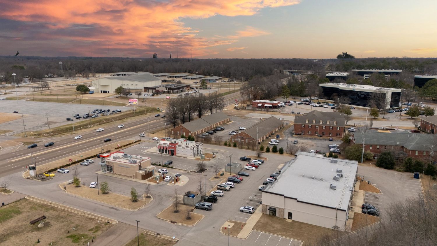 A panoramic aerial view of a commercial district with buildings and parking lots at sunset with orange clouds.