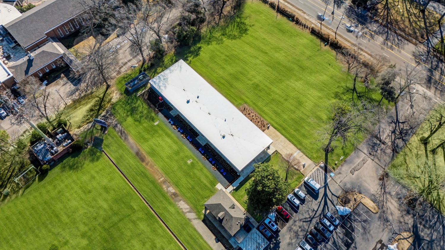 Aerial view of a lush green sports field with surrounding trees and buildings on a sunny day.