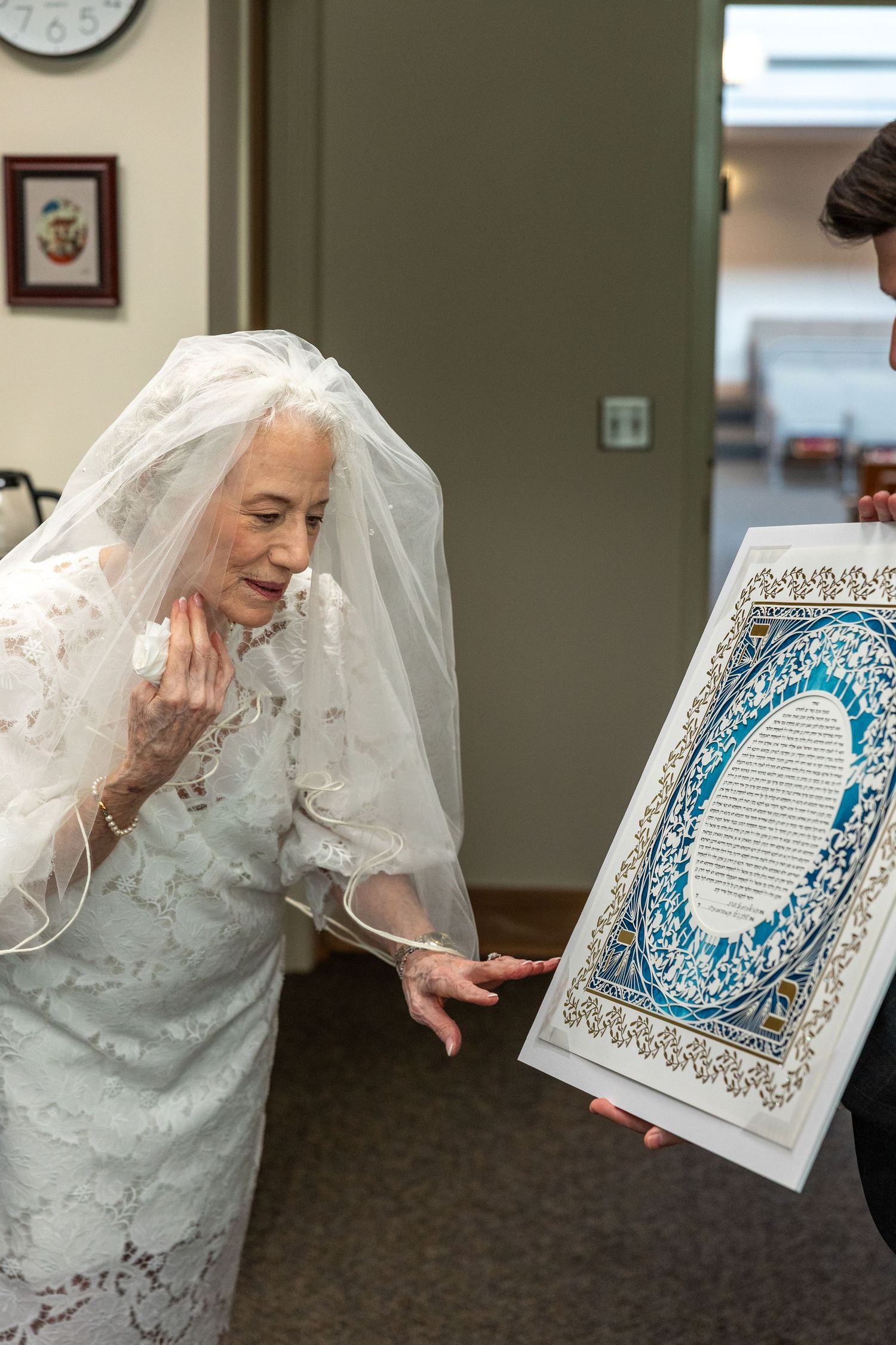 A person in white lace reacts emotionally while reading a decorative blue and white ketubah marriage document.