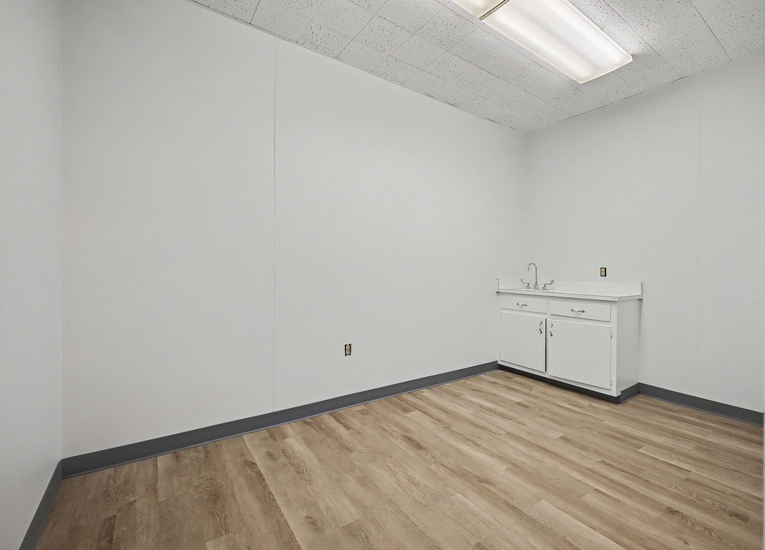 Empty commercial office space with white walls, fluorescent lighting, and new light wood flooring.