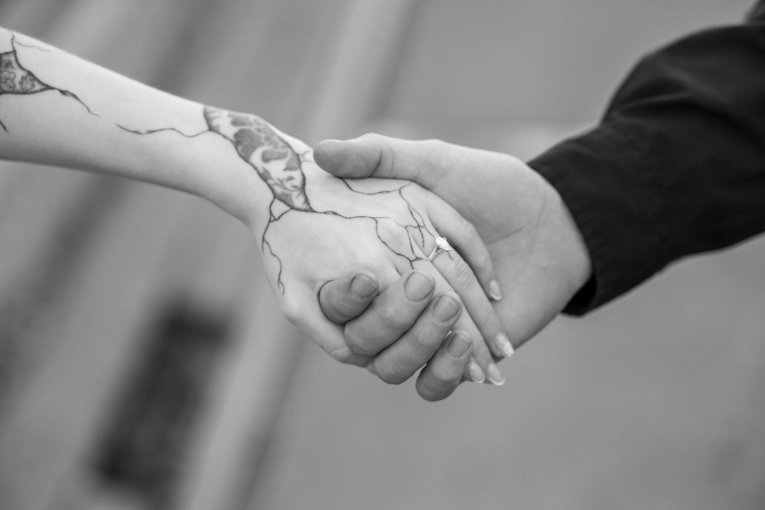 Black and white image of two hands clasped in a handshake, with one hand showing intricate tattoo artwork.