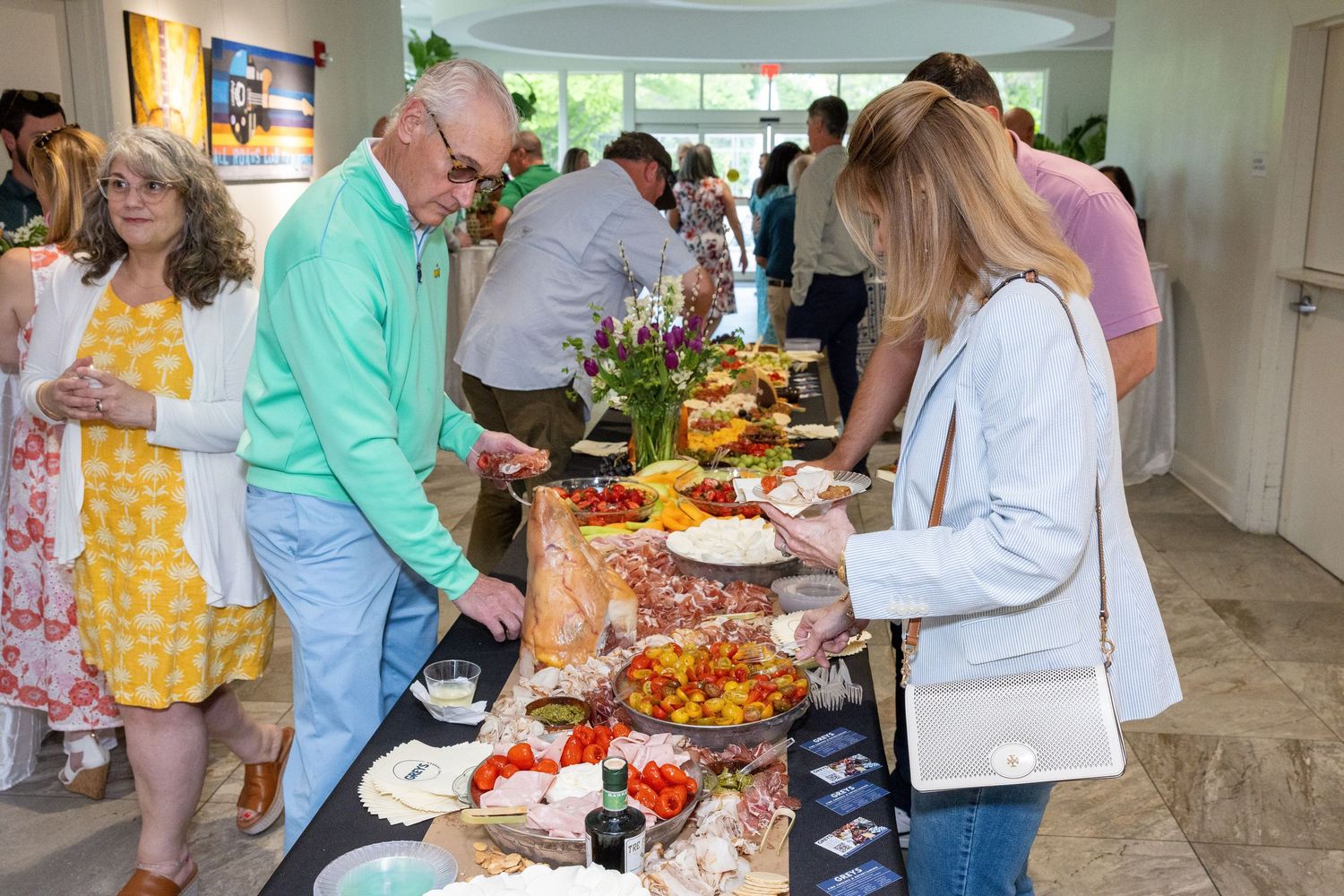 Guests enjoying a buffet spread at an elegant indoor party with fresh flowers and colorful food platters.