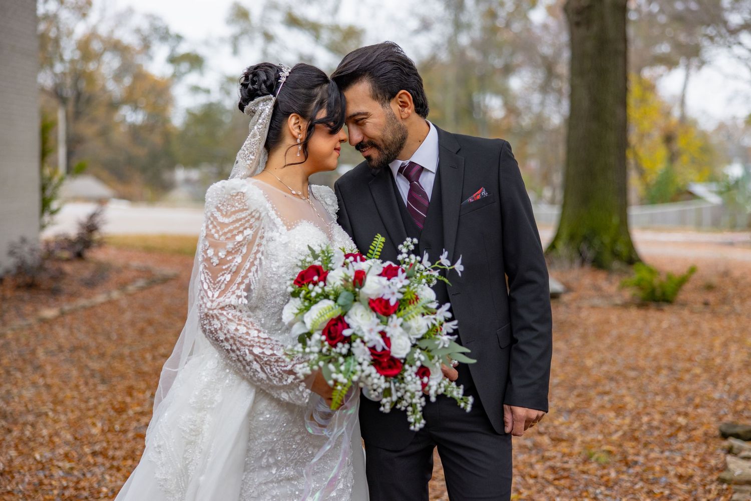 Autumn wedding portraits with fallen leaves and trees creating romantic backdrop.