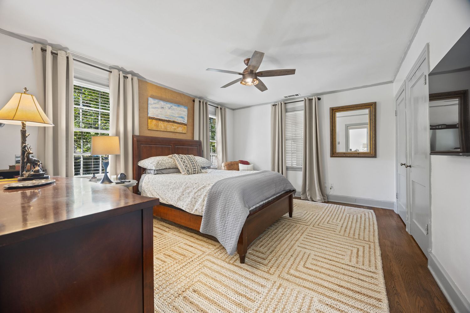 Modern bedroom with dark wood furniture, geometric rug, and natural light from windows.