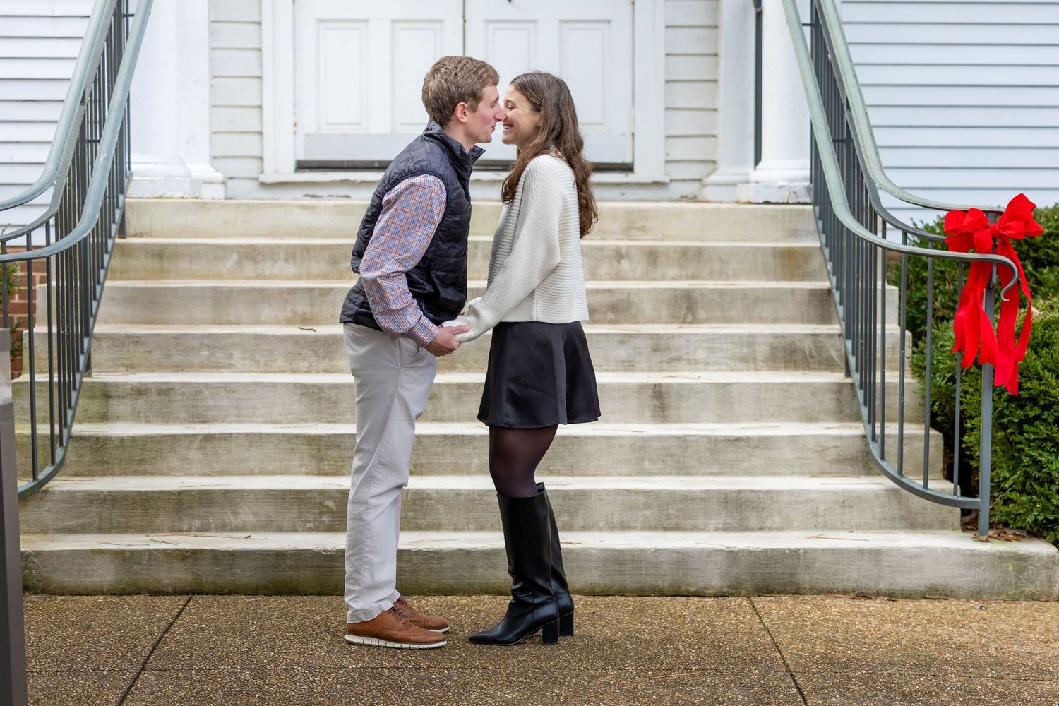 A romantic moment shared on white stone steps with holiday decorations and iron railings.