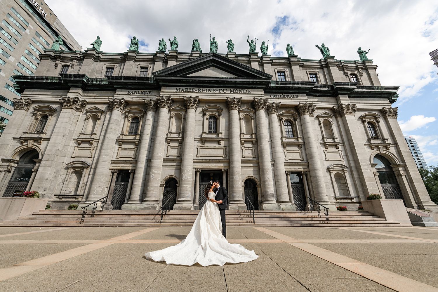 Bride and groom pose in front of a grand historic stone cathedral with sweeping white wedding gown train.