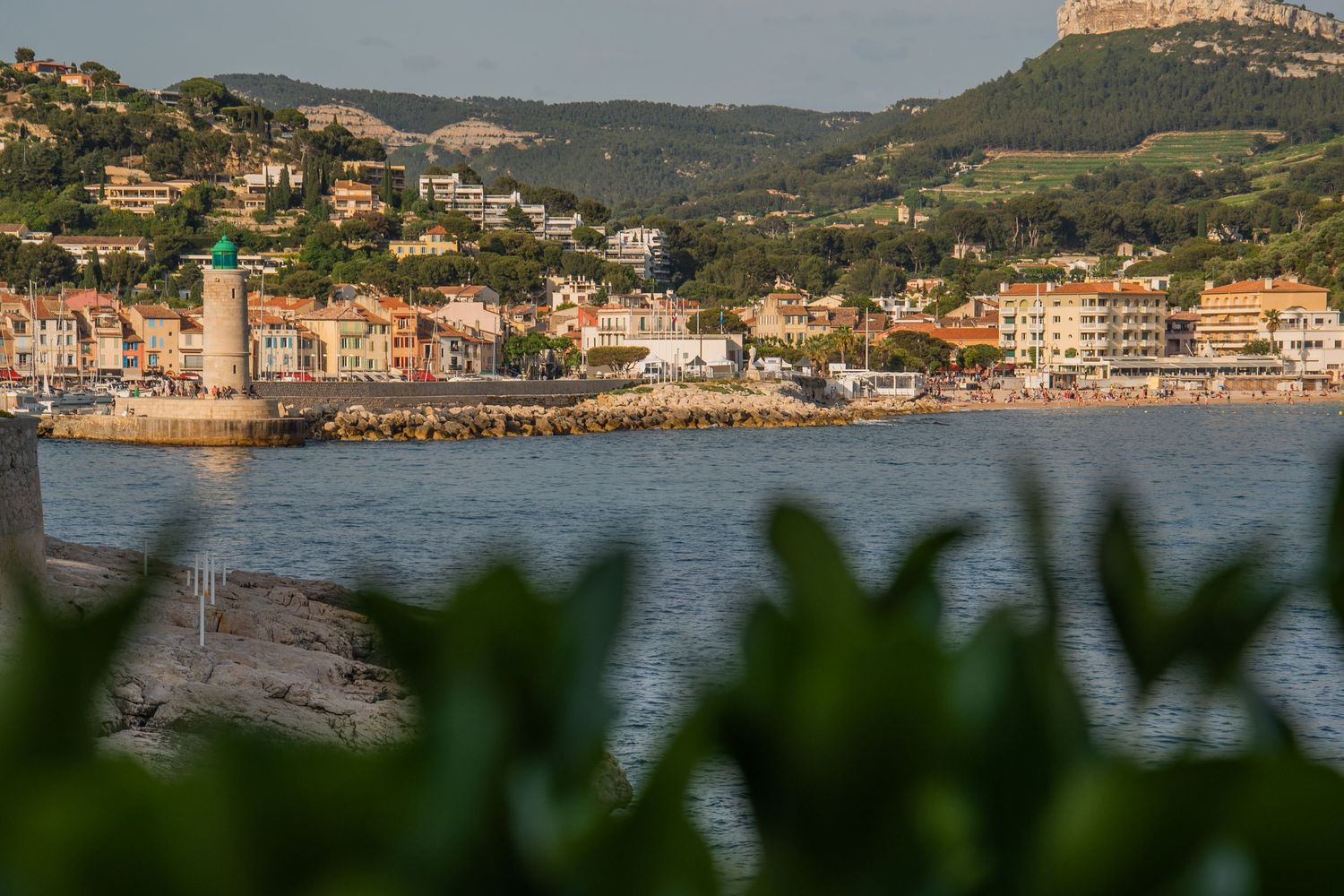 Panoramic coastal view of a Mediterranean seaside town with colorful buildings nestled against green hills and blue water.