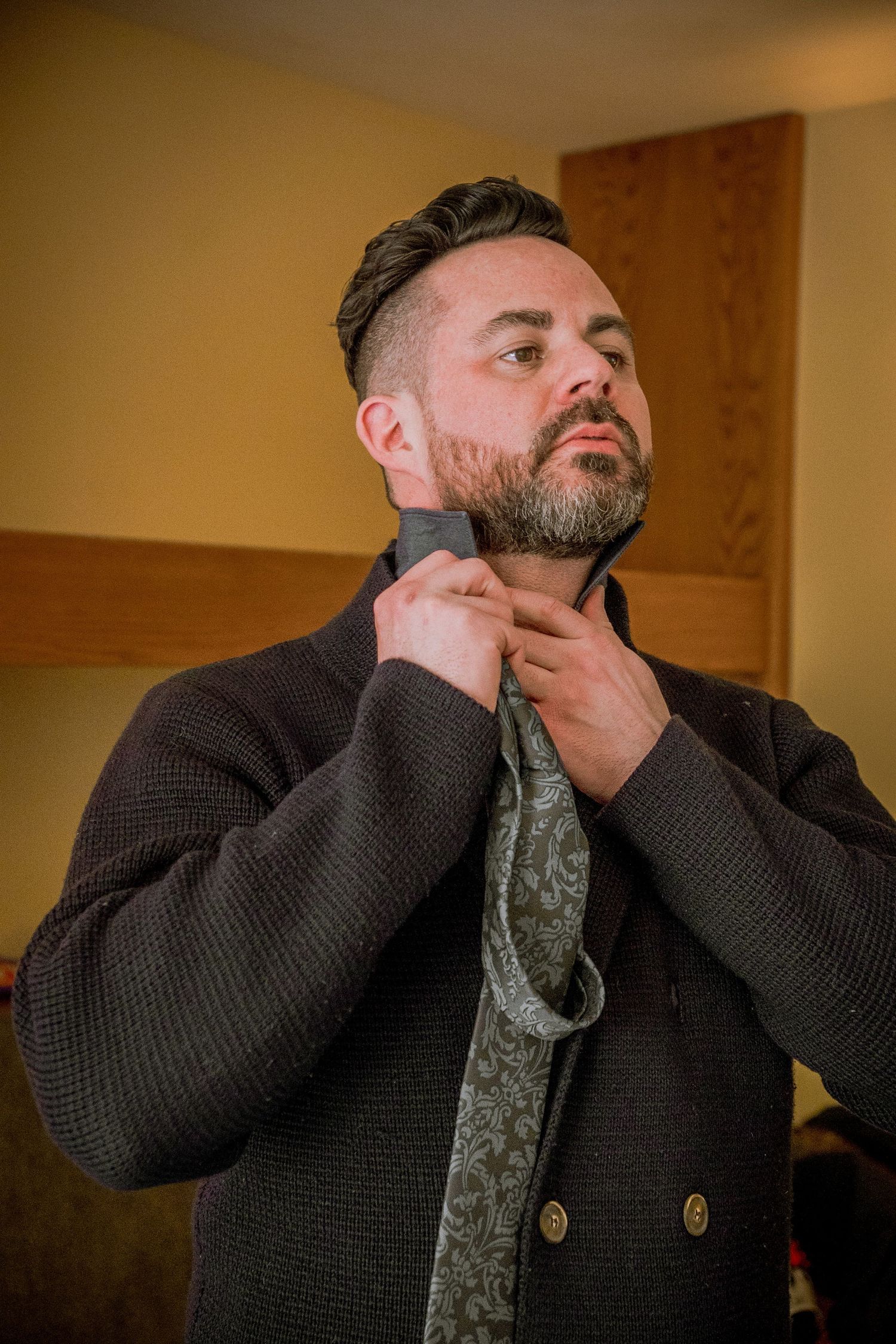 Person in dark knit sweater adjusts collar in sequence of progressive shots showing styling motion.