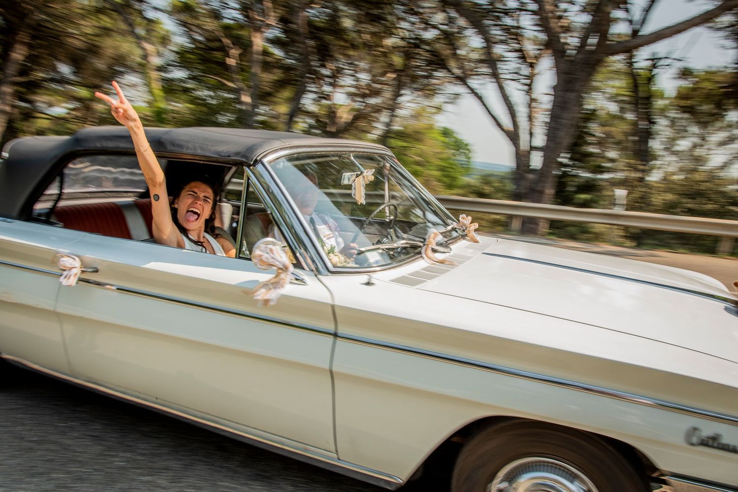 A classic white convertible car drives along a scenic coastal road with ocean views in the background.