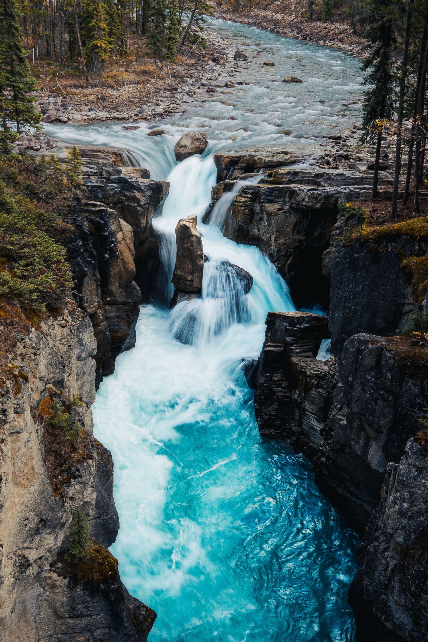 Stunning turquoise waterfall cascading through rocky canyon walls in a pristine wilderness landscape.