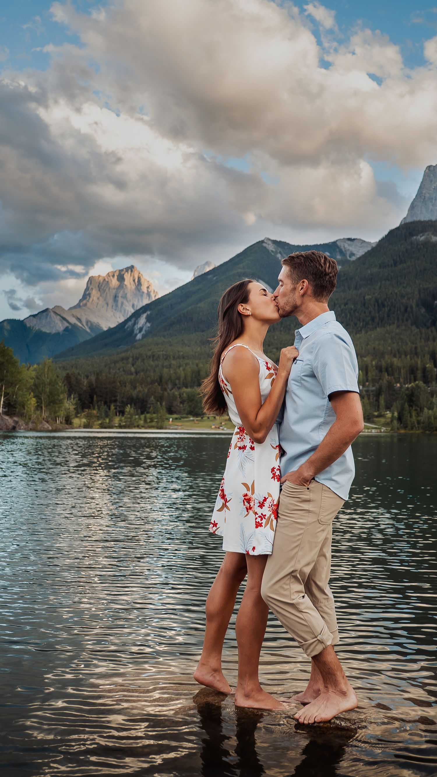 Couple standing in lake water with mountain backdrop during sunset.