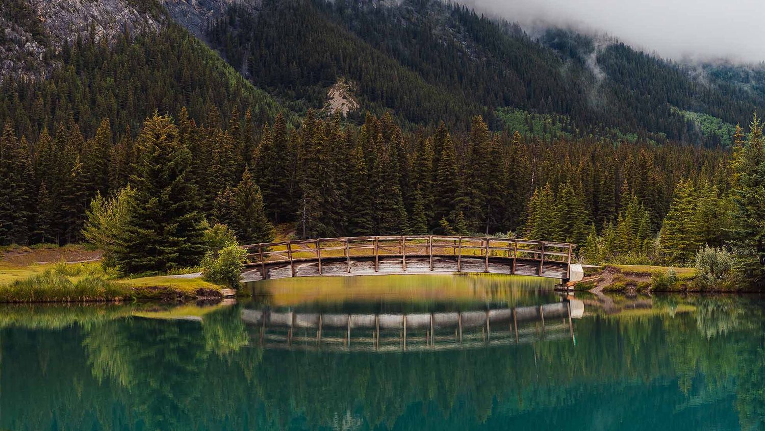 A panoramic view of a mountain lake surrounded by evergreen forest and wooden bridges in Banff National Park.