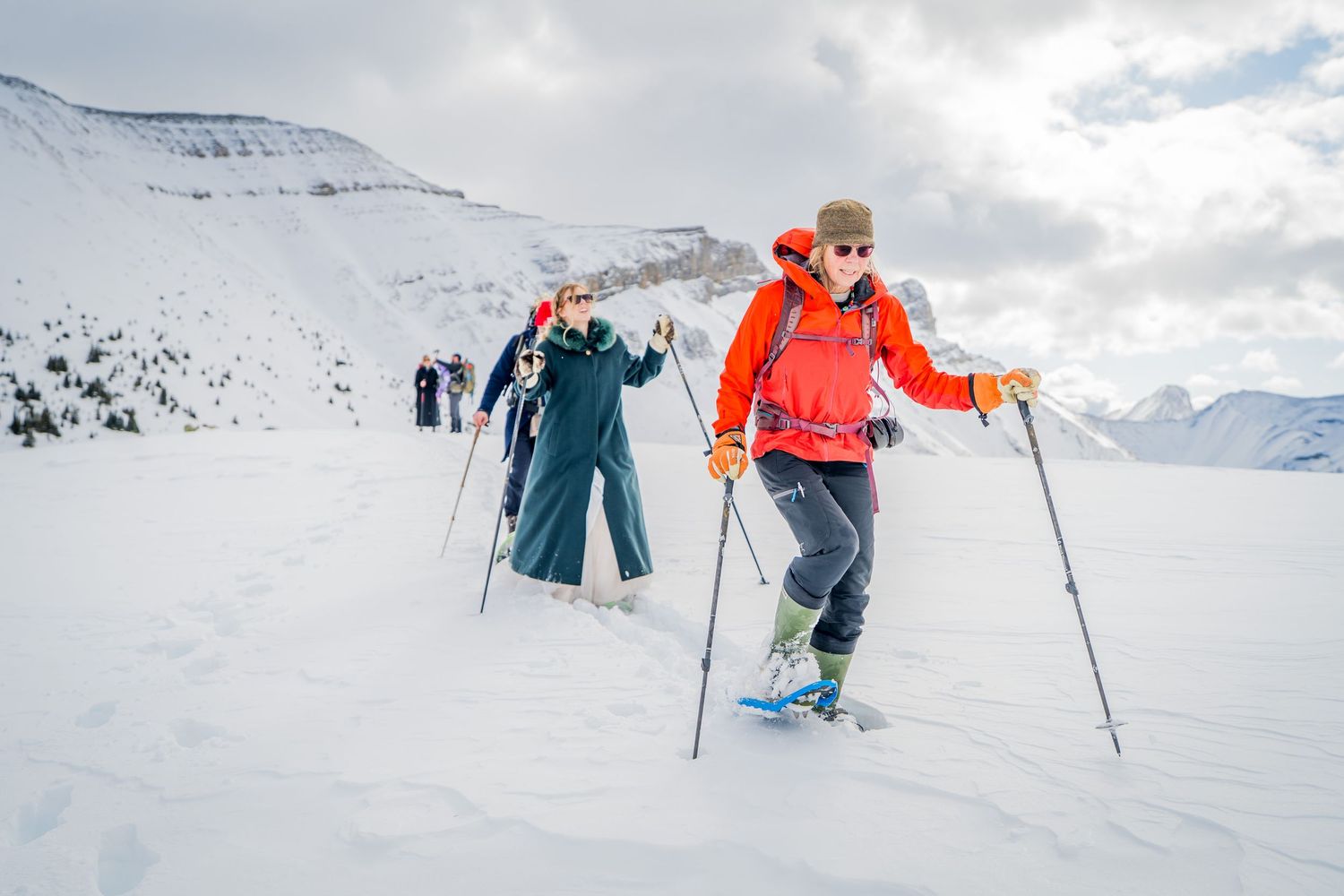 Group of skiers hiking uphill through snowy mountain terrain using ski poles on a cloudy winter day.