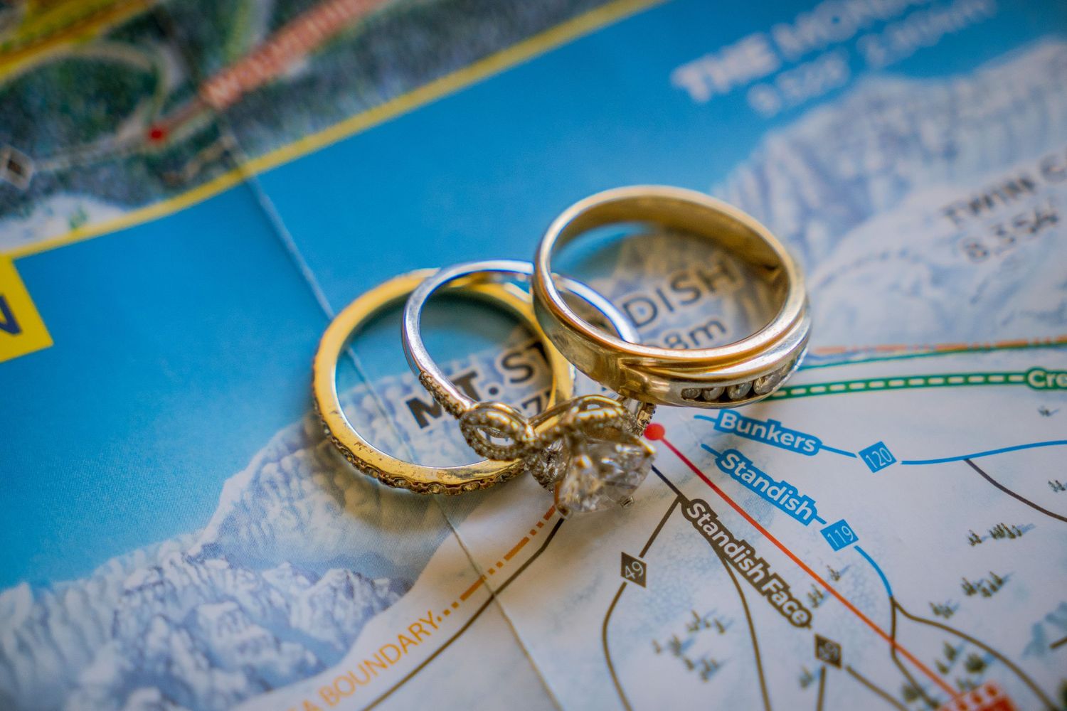 Wedding rings rest on a blue map, symbolizing travel and adventure in marriage.