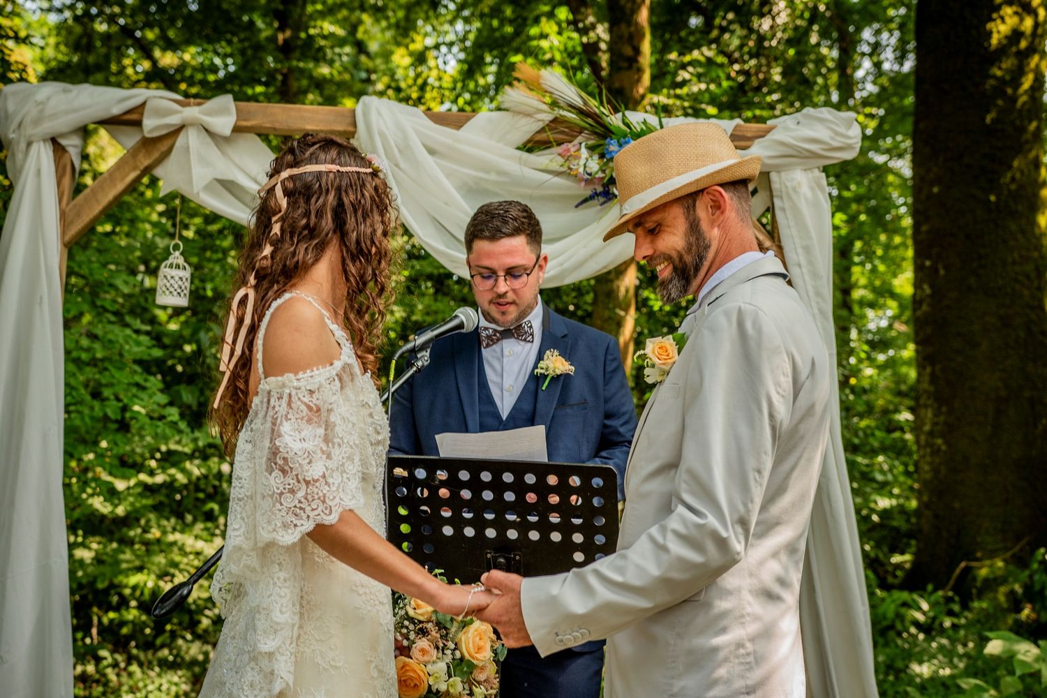 Outdoor wedding ceremony takes place in a lush green garden setting with white fabric draped decorations.
