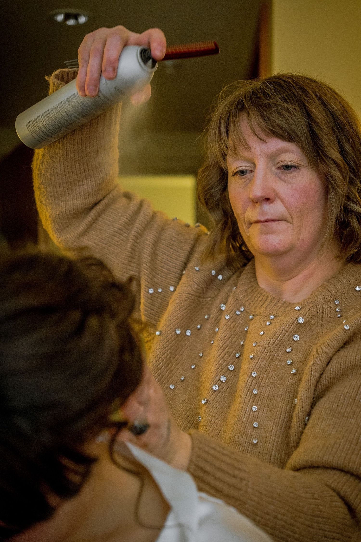 Person wearing a beige sweater with sparkly embellishments raises their hand in an indoor setting.